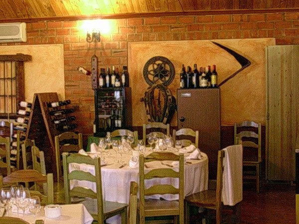 El comedor: mesas con mantel blanco, sillas de madera, pared de ladrillo y botelleros